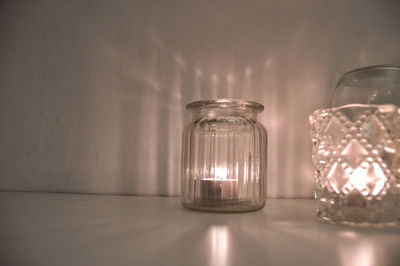 Close-up of candle in jar on table against wall