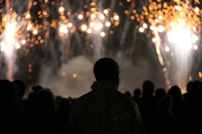 Silhouette people standing on field during firework display at night