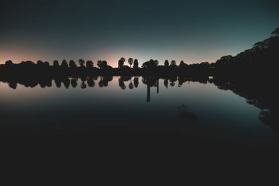 Reflection of silhouette trees in lake against clear sky