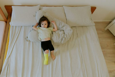 A baby girl with a cast on her leg lies on the bed.