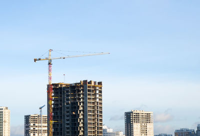 Low angle view of crane and buildings against sky