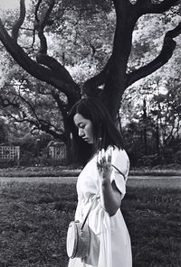 Portrait of young woman standing by tree trunk in park