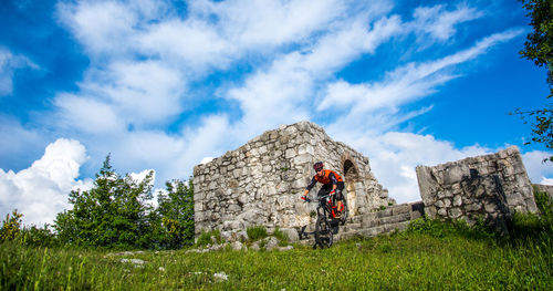 Low angle view of man with bicycle against cloudy sky