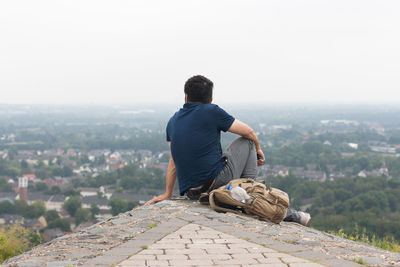 Rear view of man looking at cityscape while sitting against sky