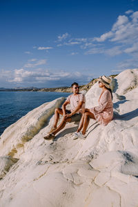 People sitting on shore at beach against sky