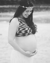 Smiling pregnant woman touching abdomen at beach