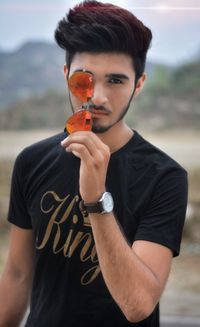 Portrait of young man holding sunglasses standing on field