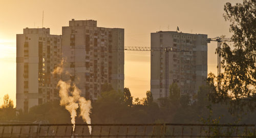 Smoke emitting from factory against sky during sunset