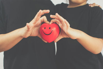 Midsection of couple holding red heart shape with anthropomorphic face