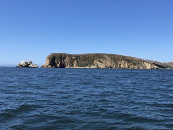 Rock formation in sea against clear blue sky