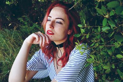 Beautiful young woman with redhead sitting amidst plants in park