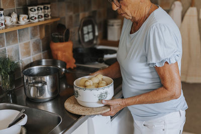 Senior woman in kitchen holding bowl with boiled potatoes