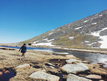 Rear view of woman walking by lake against clear blue sky