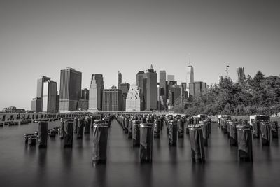 Wooden post in east river by modern city skyline against clear sky