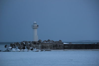 Lighthouse by sea against clear sky during winter