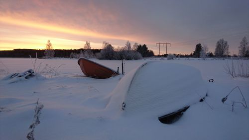 Snow covered landscape against sky during sunset