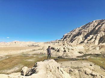 Rear view of man standing on mountain against clear blue sky