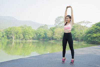 Full length of young woman exercising on road by river at park