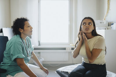 Young woman showing ear to female physician while sitting in clinic