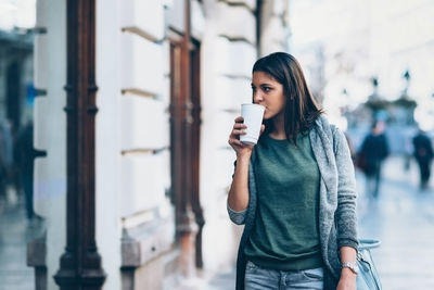 Young woman drinking coffee while looking away in city