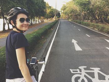 Smiling woman with bicycle on street amidst trees