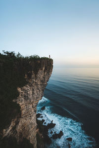 Cliff by sea against clear sky during sunset