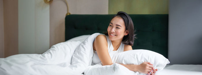 Portrait of young woman sitting on bed at home