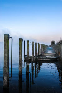 Wooden posts in lake against clear blue sky