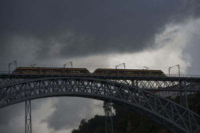 Low angle view of train on arch bridge against cloudy sky