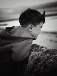 Boy looking away by wall against sky