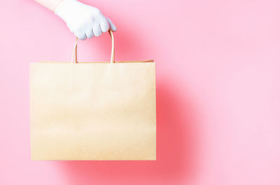 Female hand in glove holds a cardboard bag on a pink background, food delivery concept.