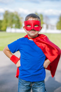 Portrait of boy in superman costume standing on road against sky