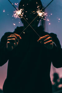 Close-up of man holding illuminated fireworks against sky at night