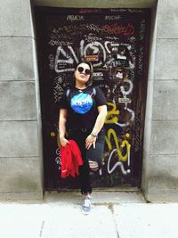 Portrait of woman standing against graffiti wall