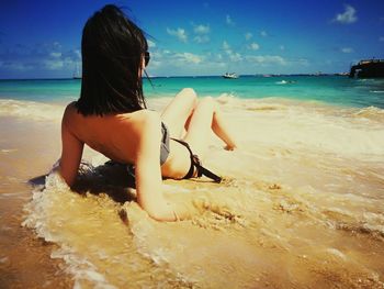 Young woman sitting on shore at beach against sky