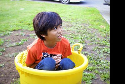 Boy looking away while sitting in yellow container on land