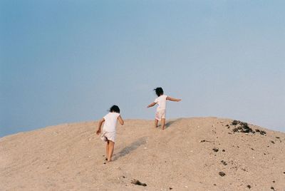 Rear view of friends walking on sand against clear sky