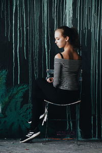 Woman sitting on chair against wall