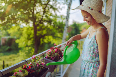 Woman watering plants with can while standing in balcony