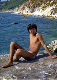 Portrait of shirtless man sitting on rock
