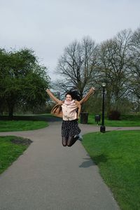 Full length of woman jumping with arms raised in park
