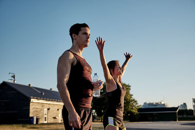 Young man with arms raised against clear sky