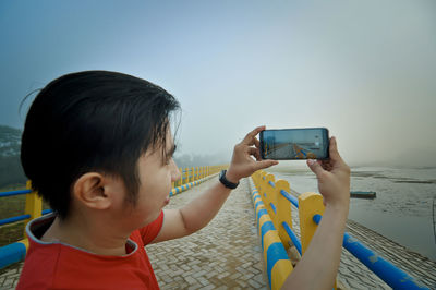 Rear view of boy photographing with mobile phone