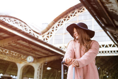 Beautiful young woman in black hat and pink coat with suitcase stands