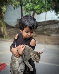 Cute little girl holding cat standing outdoors