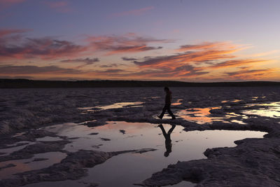 Silhouette of a person walking through a saltworks area at sunset