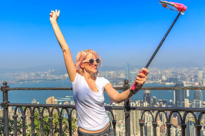 Woman taking selfie with mobile phone against cityscape