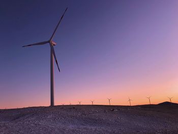 Wind turbines on field against sky during sunset