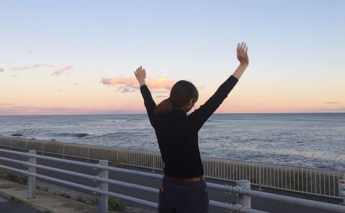 Woman with arms raised standing at beach against sky during sunset