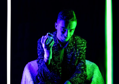 Young man looking away while sitting against black background